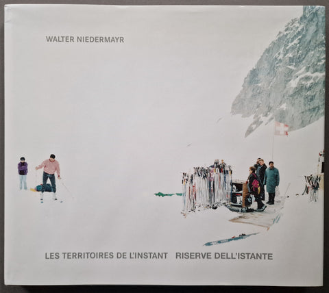 A square art book cover featuring a snowy mountain scene with skiers and a group of people standing near ski racks. The top left reads 'WALTER NIEDERMAYR' and the bottom reads 'LES TERRITOIRES DE L'INSTANT RISERVE DELL'ISTANTE'.