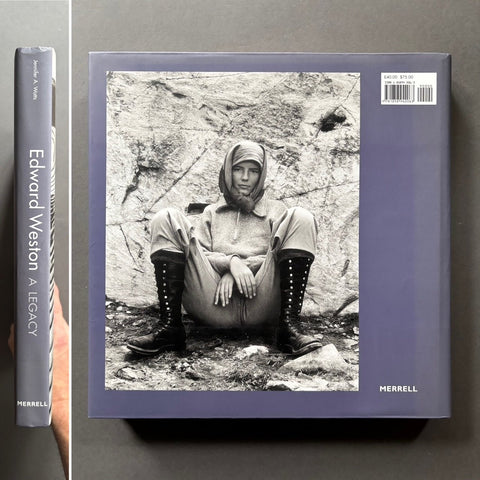 Book cover with a black and white photo of a person sitting on rocks, held by a hand.