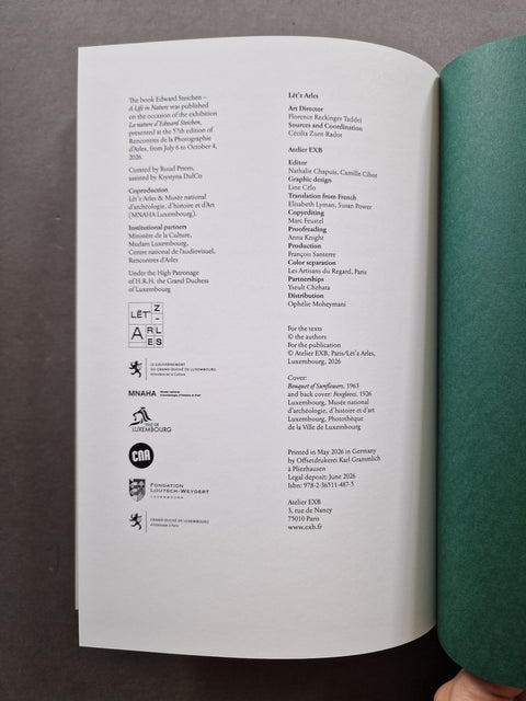 An open book or booklet showing printed text and small logos on a white page, with a green cover or folded page visible at the top, photographed on a dark gray surface.