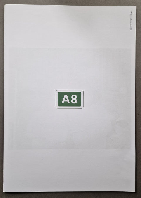 A white A8 paper newspaper publication cover centered on a dark gray surface, with a green and white 'A8' sign in the middle.