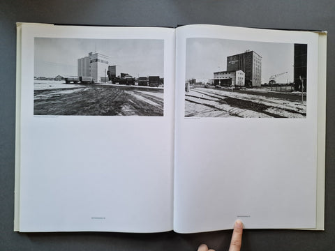 An open book showing two black-and-white architectural photographs printed on the pages, photographed from above on a dark gray surface.