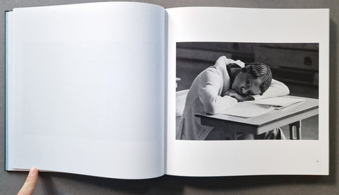 An open book, showing a large blank left page and a black-and-white photograph on the right page of a person leaning on a desk.