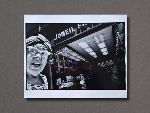 A black and white photographic art print featuring a woman screaming in front of a store sign that reads 'JONEIL' displayed against a textured gray background.