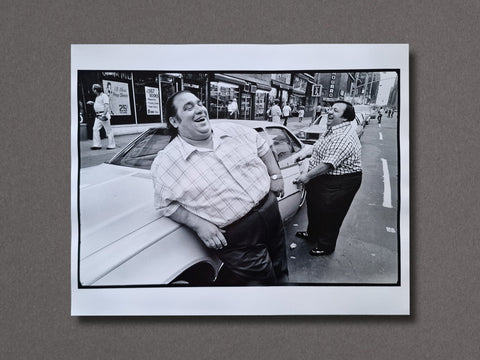 An art print picturing two men of heavy built in checkered shirts laughing, one is leaning on a white car while the other one has opened the door of the same car and about to enter.