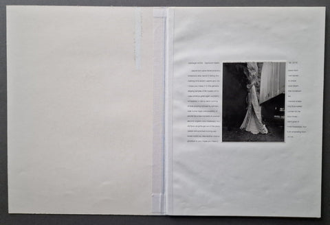 An open white art book , showing a black-and-white photograph on the right page with surrounding text, photographed against a dark gray background.