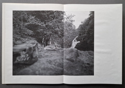 An open book showing a black-and-white photographic print of a forest trail scene with people walking among rocks and trees.