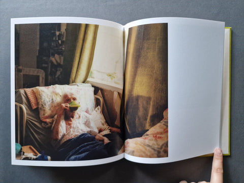 An open hardcover book, showing a photographic print of a person lying in bed spread on both pages.