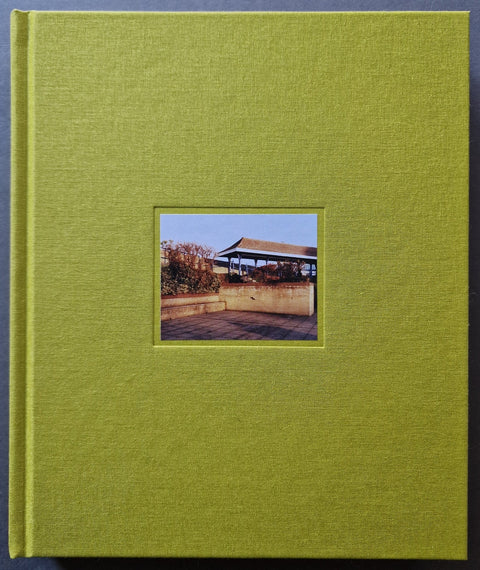 A square hardcover book cover in textured olive green, featuring a small centered inset photograph of an outdoor pavilion scene.