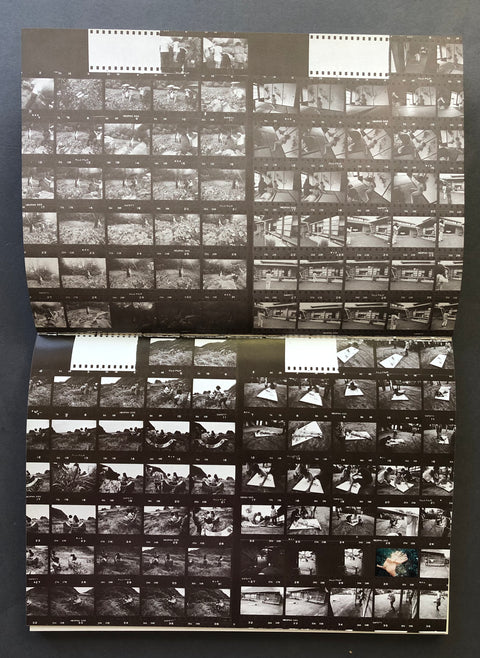A vintage black-and-white film photo album or binder spread open on a dark surface, showing multiple printed film strips with numerous small black-and-white photographs arranged in a grid.