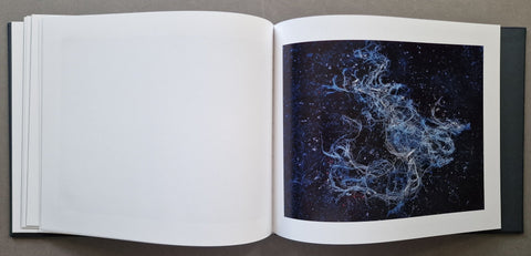 An open book or art print showing a blank white left page and a right page with a square black-and-white cosmic photograph of swirling nebulae in space.
