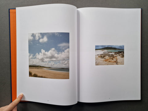 An open hardcover book - The left page shows a beach landscape photo under a cloudy blue sky, and the right page has a smaller coastal scene photo.