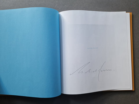 An open book, showing a bright blue left page and and a right title page with Kenna's signature