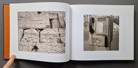 An open book, showing two printed photographs on the pages: a close-up of rough stone on the left and an old wall-mounted phone on the right. A hand is holding the left page.
