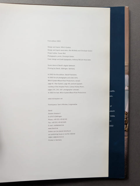 A printed book page shown from the back, with dense black text on a white sheet and a dark blue spine or binding edge visible along the right side against a gray background.