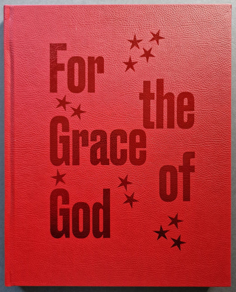 A red textured book with embossed dark red text reading 'For the Grace of God' and small star motifs, shown against a neutral gray background.