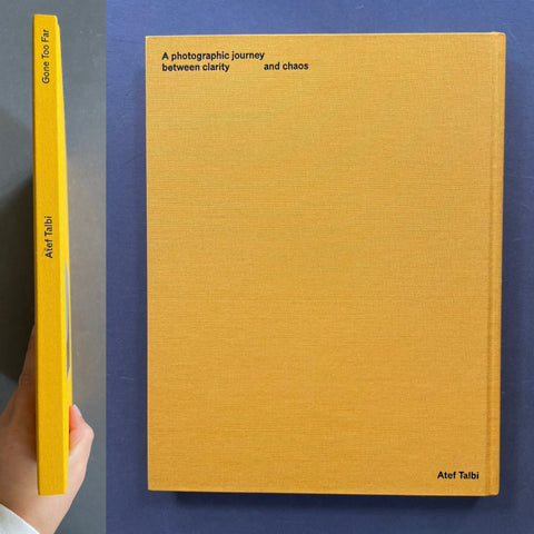 A hardcover book titled 'A photographic journey between clarity and chaos' by Atef Talbi, shown standing upright with its front cover and spine visible against a dark blue background. A hand is holding the left edge of the spine to show thickness.