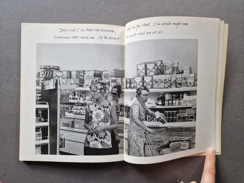 An open book. The pages show a black-and-white photograph of people in a grocery store aisle with handwritten text at the top of the left page.