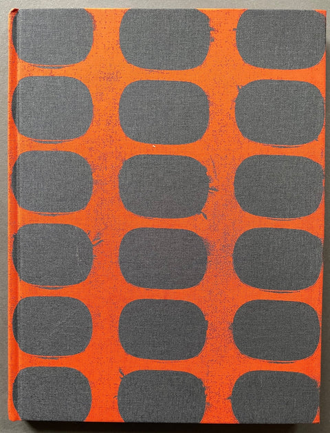 A hardcover book or journal with a textured orange cover featuring a repeating pattern of dark gray rounded rectangles, photographed flat against a neutral gray background.
