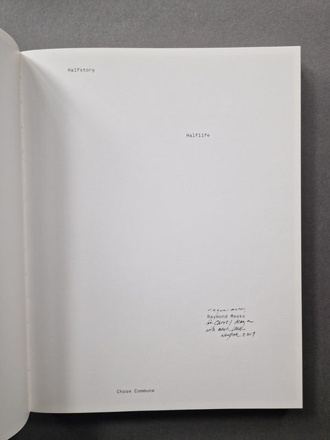 An open book or booklet showing a large white interior page with small printed and handwritten text, photographed against a dark gray background.