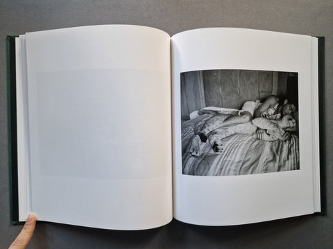 An open hardcover book, showing a black-and-white photograph printed on the right page and blank white pages on the left. The photo is of a man lying in bed next to a big wild cat