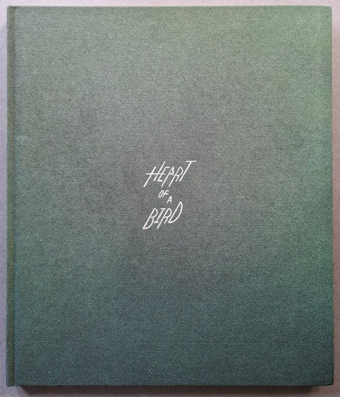 A square hardcover book with a textured green surface and the title 'Heart of a Bird' printed in white script near the center.