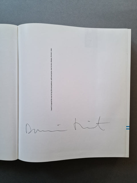 An open book, showing a mostly blank white page with a small vertical block of text and a handwritten signature near the bottom.