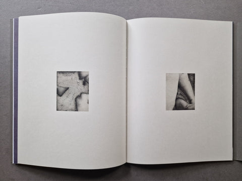 An open book showing two white pages with small black-and-white square photographs of body parts centered on each page.