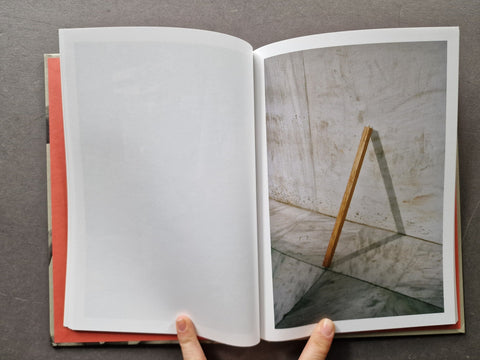 An open book showing a blank white page on the left and a photograph of a wooden easel leg against a textured wall on the right
