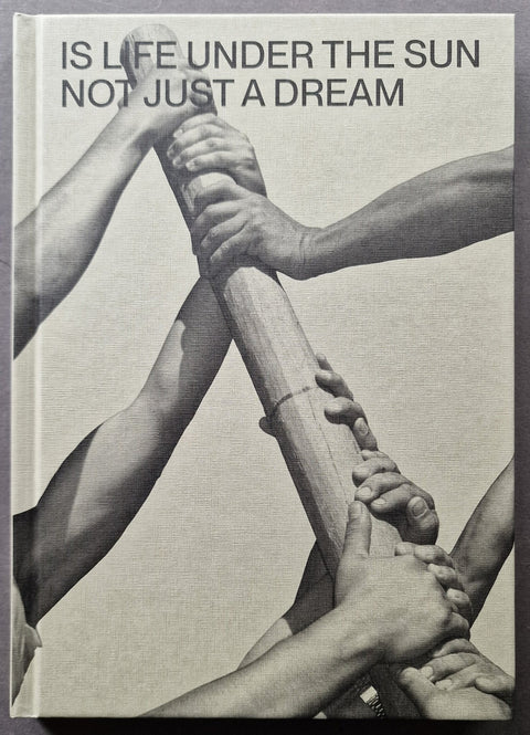 A square book cover featuring a black-and-white photograph of multiple arms gripping a wooden pole together, with the text 'IS LIFE UNDER THE SUN NOT JUST A DREAM' at the top.