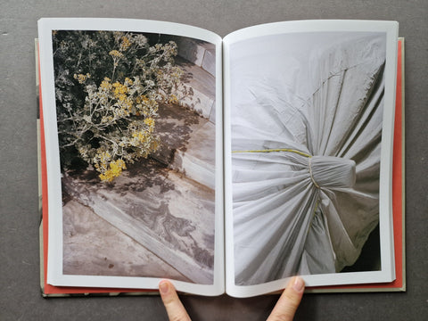 An open book showing two photographic pages: one with dried yellow flowers on stone, and the other with a close-up of white draped fabric.