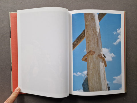 An open book, showing a blank white page on the left and a printed photograph on the right of a person climbing a large wooden post against a blue sky.
