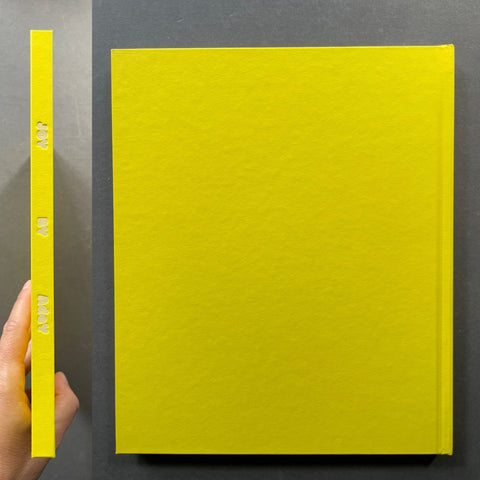 A bright yellow hardcover book or journal shown standing upright, with a hand holding the spine on the left to demonstrate its thickness. The cover is textured and features the title 'THE ART OF AI' embossed vertically on the spine.