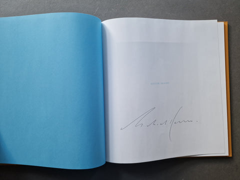 An open book, showing a bright blue left page and and a right title page with Kenna's signature
