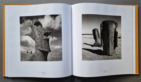 An open book showing two black-and-white photographic prints of Moai statues on a grassy landscape under a cloudy sky.