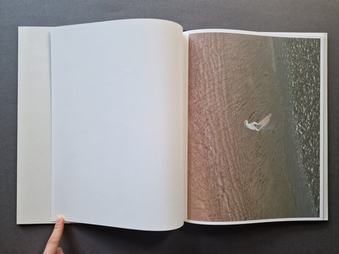 A book spread showing a large-scale negative of a person on the beach looking in the water on the right page