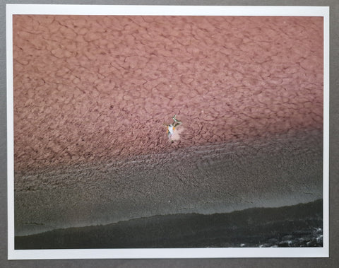 A square art print with a white border, depicting a close-up textured landscape with a dusty pink upper area, a darker gray middle band, and a dark near-black lower band. The print is photographed against a neutral gray background.