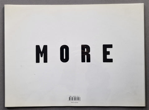 A minimalist back cover featuring the word 'MORE' in bold black sans-serif letters on a white background, photographed flat against a dark gray surface.