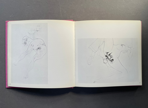 An open sketchbook or art print book laid flat on a dark gray surface, showing two white pages with faint pencil line drawings of human figures.