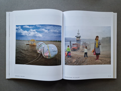 An open book showing two printed photo pages side by side. The left page contains a landscape photo of inflatable floating domes on water, and the right page shows a dusty outdoor scene with people and a vehicle.