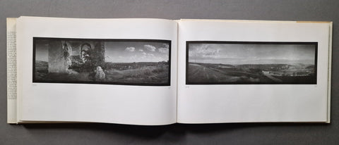 An open book displaying two panoramic black-and-white landscape photographs printed on white pages, photographed against a dark gray background.