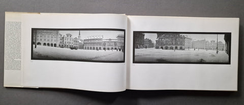 An open book showing two black-and-white panoramic architectural photographs printed on white pages, photographed against a dark gray background.