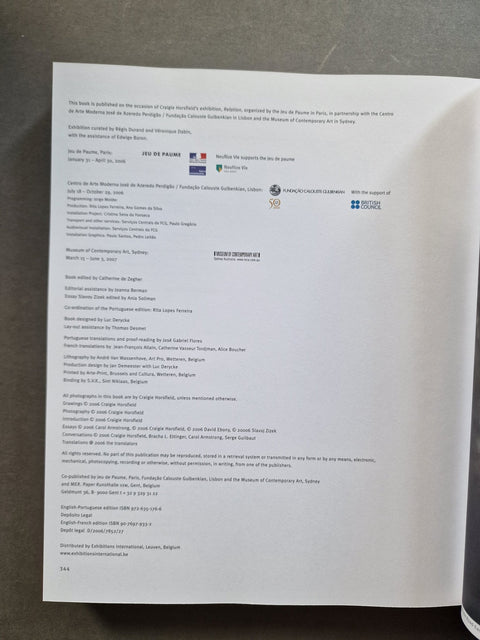 A printed document or booklet page photographed from above on a dark gray surface, with dense small text and several small logos or flags visible near the top left.