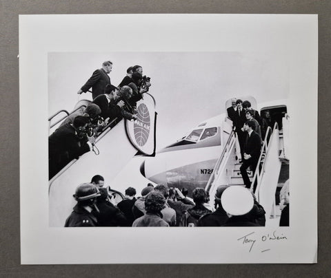 A black and white signed silver gelatin print of The Beatles getting on an airplane, Terry O'Neill's signature in the bottom right corner