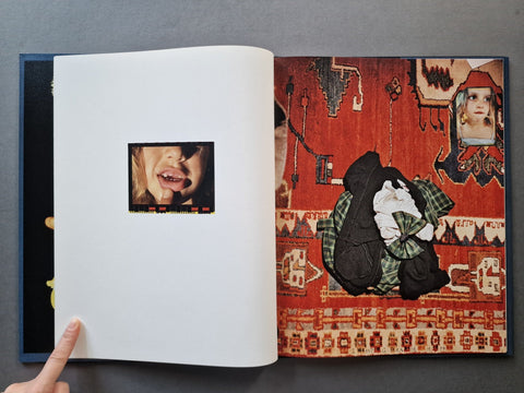 An open art book, showing a white left page with a small portrait inset and a right page with a complex collage design featuring a red patterned rug, a black hat, green plaid fabric, and a child's face.