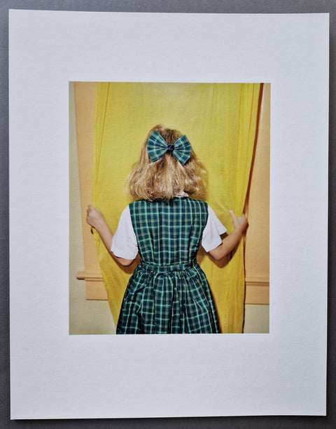 The photographic print portraying Ruby Goldberg with her back to the camera in green gingham uniform and a matching bowl holding a yellow window drape.