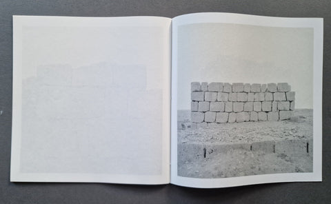 An open book, showing a mostly blank left page and a grayscale photograph of stacked stone blocks on the right page.