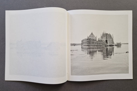An open book, showing a monochrome photograph of a floating structure on water printed on the right page, with blank white paper on the left page.