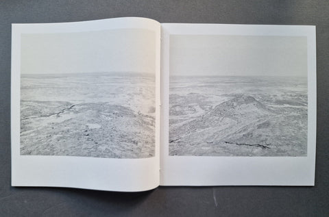 An open book showing two grayscale landscape photographs side by side on a dark gray surface.