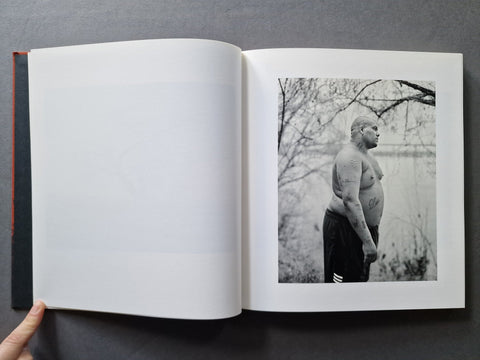 An open hardcover book with a black-and-white photograph printed on the right page showing a shirtless man standing outdoors.