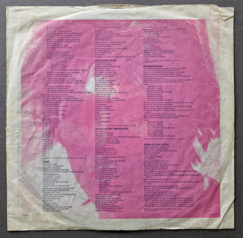 The back cover of a vinyl record sleeve for Bob Dylan's album 'The Power and the Glory', featuring a pink abstract background with white text listing track titles and credits, photographed flat on a dark gray surface.